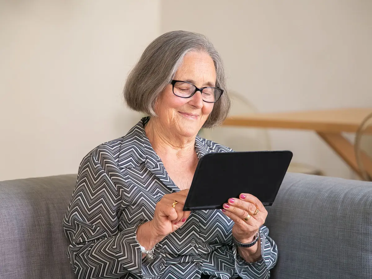 An older woman smiling as she uses a tablet
